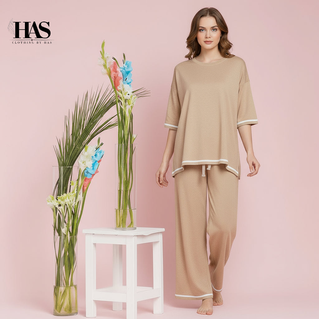 Woman in beige outfit standing next to a white stool with floral arrangements on a pink background